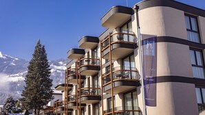 Un hotel con varios balcones, vistas a la montaña y un cartel anunciando 'Alps Resorts'.