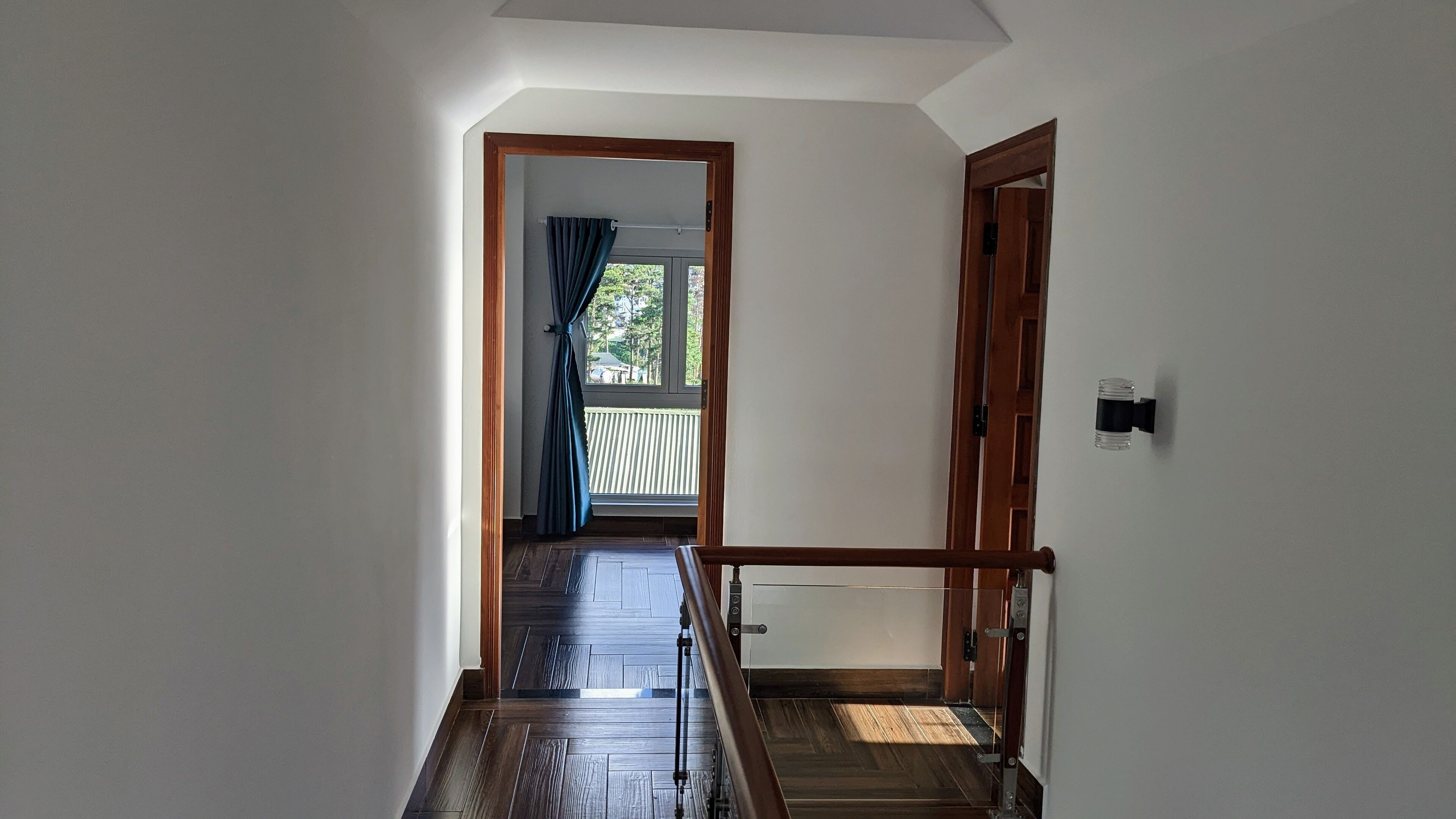 Un pasillo con piso de madera y vista a un balcón con cortinas azules.