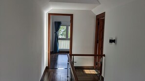 A hallway with wooden flooring and a view of a balcony with blue curtains. - VilLa 62 (Da Lat)