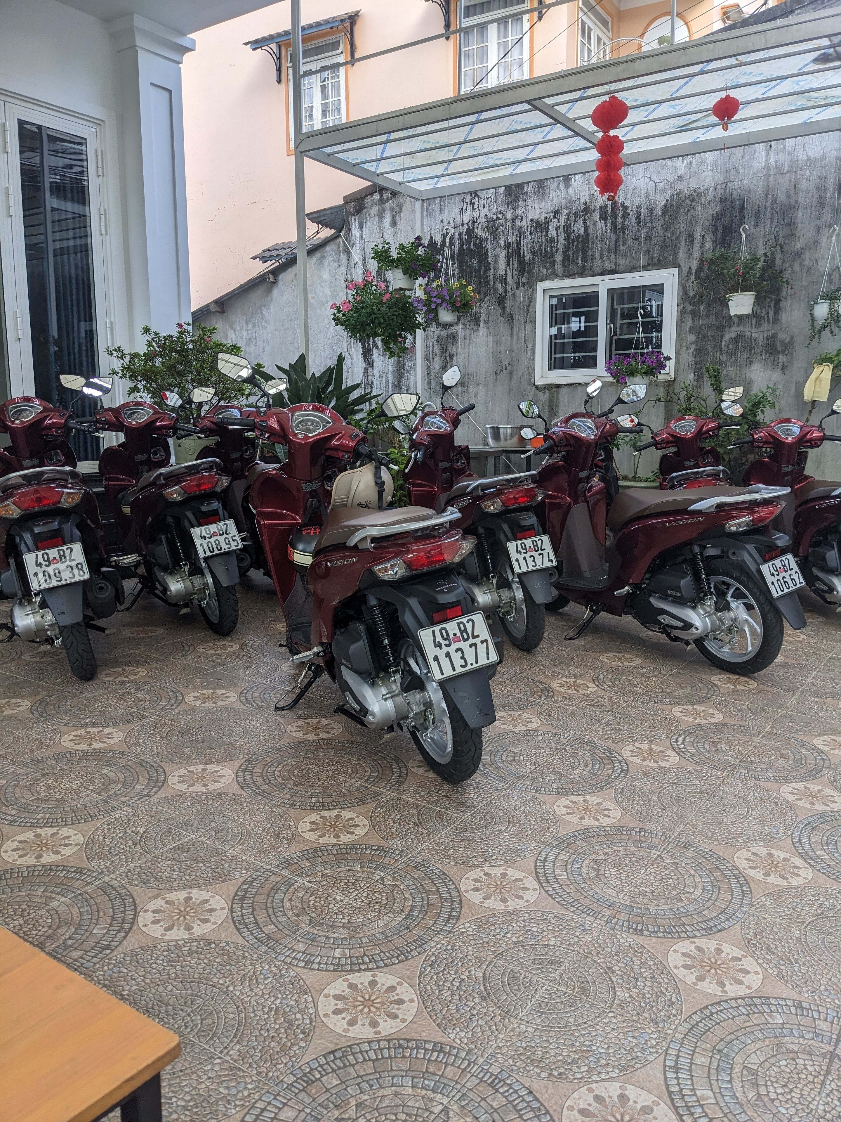 Una fila de motocicletas estacionadas, con placas de identificación, un piso de baldosas y un edificio con una ventana y una puerta al fondo.