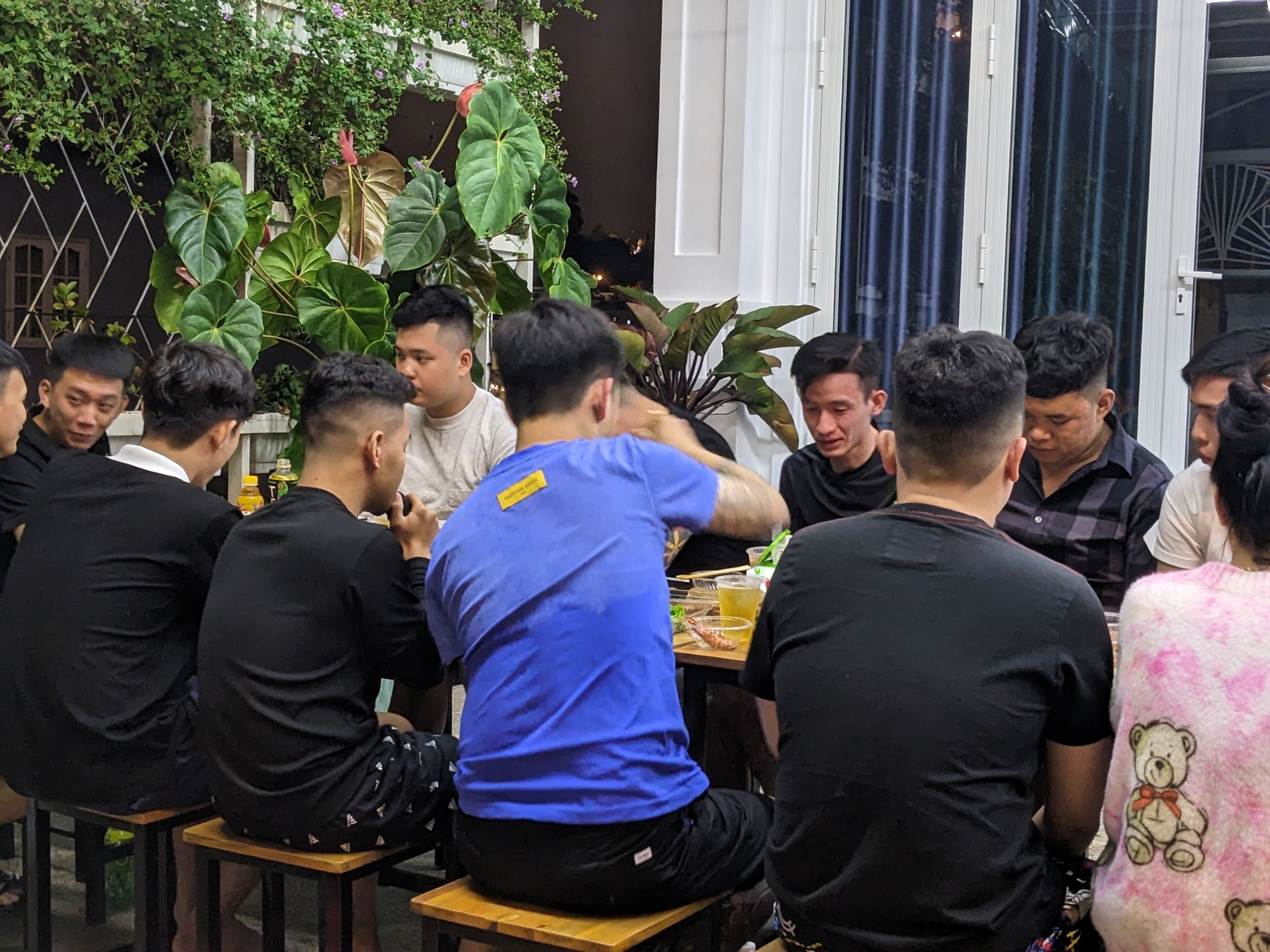 A group of people seated around a table in an indoor setting with plants and a window in the background.