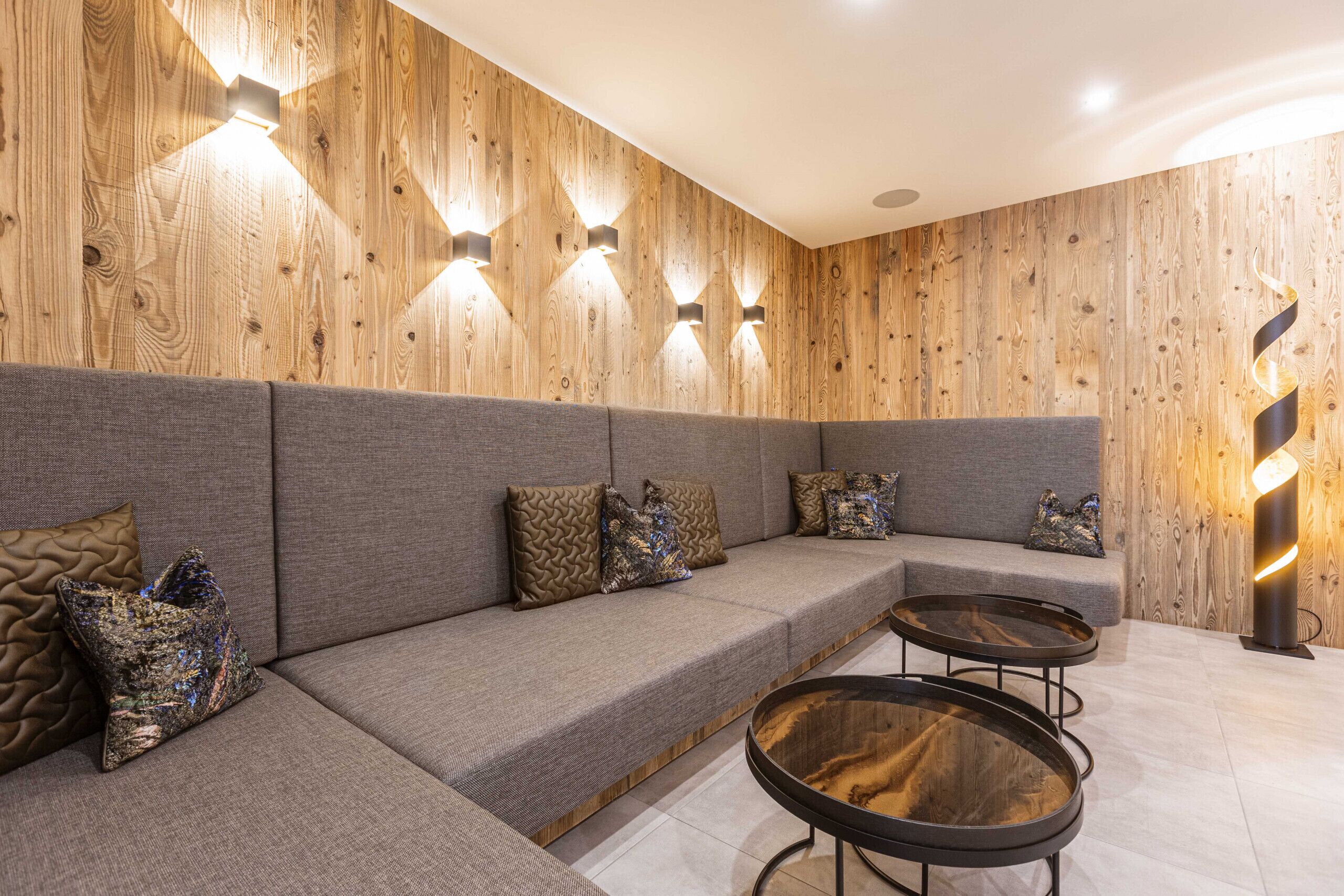 Un interno moderno con una parete in legno, un divano grigio con cuscini decorati e un tavolino rotondo.