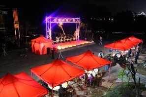 An outdoor event with a stage and seating area under red umbrellas.