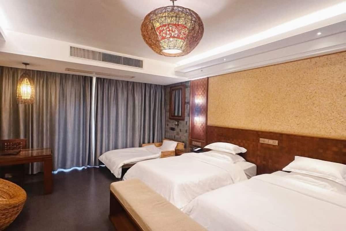 A hotel room with two beds, a bench, a table, a lamp, and a decorative wall.