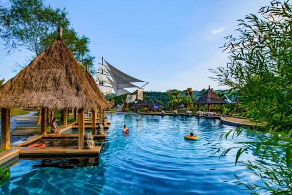 A swimming pool with a thatched-roof structure, a sailboat, and a dock with people.
