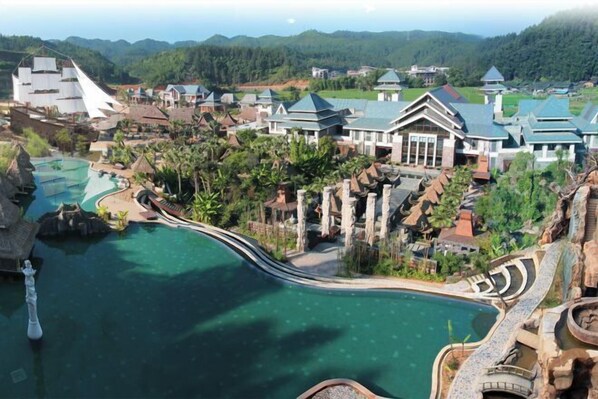 A resort with a large swimming pool, multiple buildings with green roofs, and a mountainous backdrop.