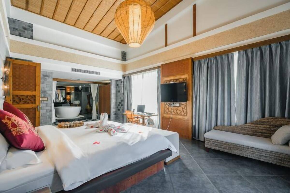A hotel room with a bed, a sofa, a television, a bathroom, and a dining area.