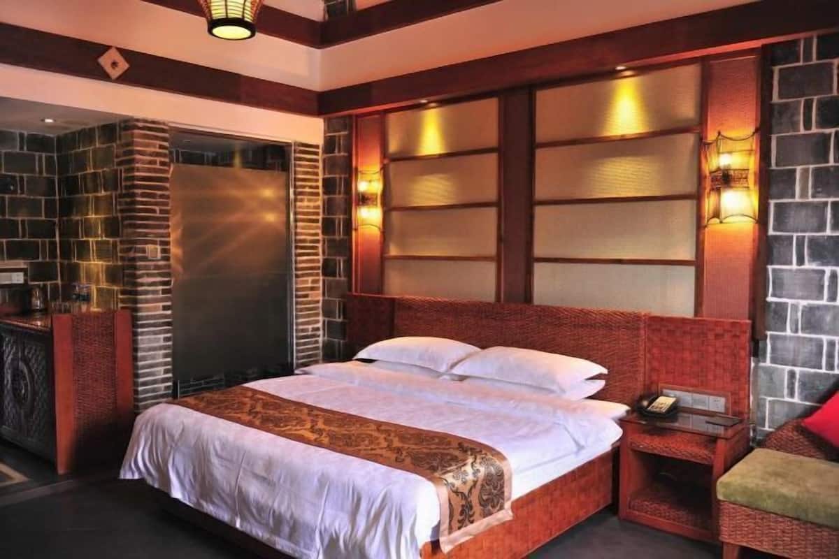 A hotel room with a large bed, a nightstand, a small table, and a seating area with a red cushion.