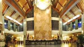 Eine großzügige Lobby mit hoher Decke, einer zentralen Rezeption und einer großen Steinwand mit Kunstwerken.