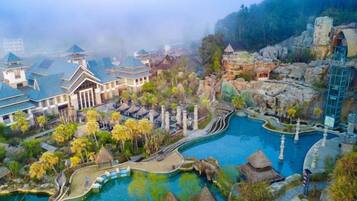 A resort with traditional architecture, a central water feature, and a mountainous backdrop.