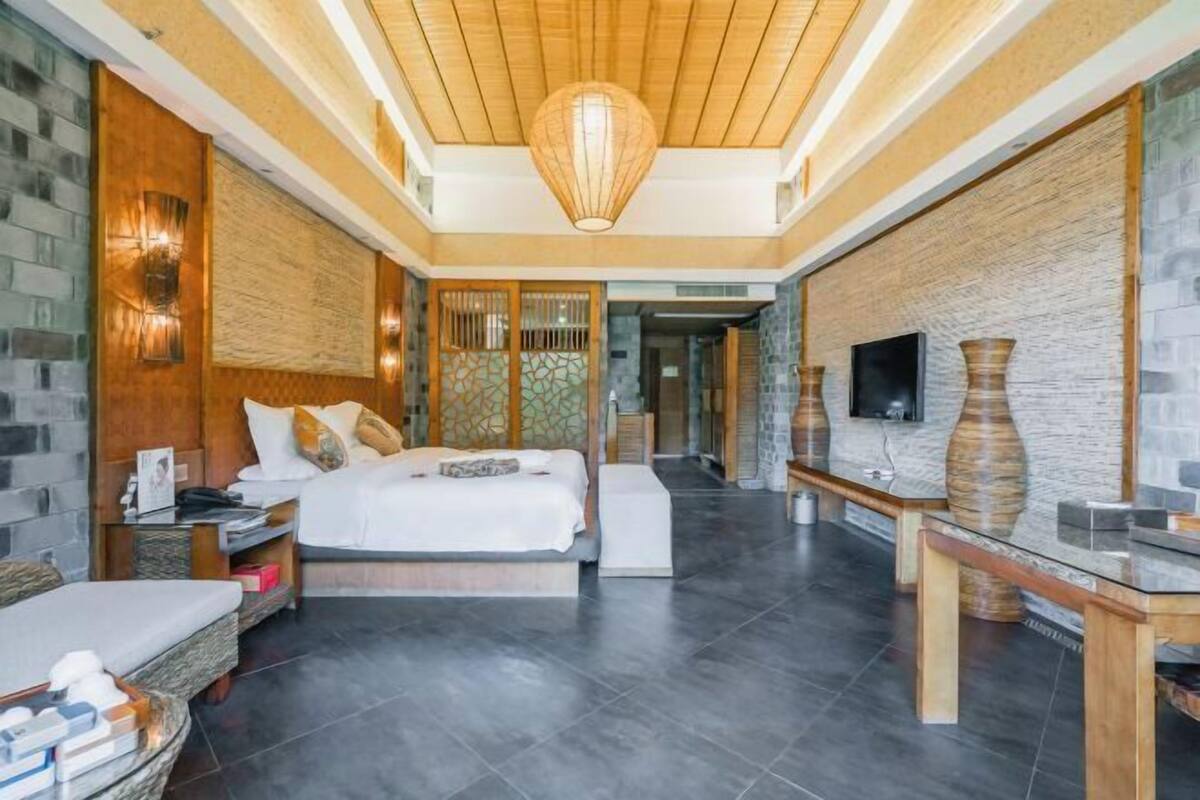 A modern hotel room with a large bed, a TV, and a wooden ceiling.
