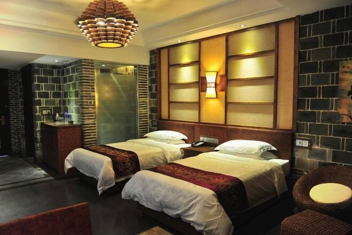 A hotel room with two beds, a wooden headboard, a wall-mounted light, and a brick-patterned wall.
