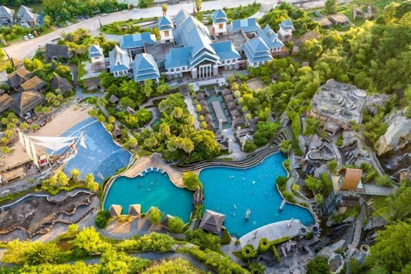 A resort with multiple swimming pools, a large building with a blue roof, and surrounding greenery.
