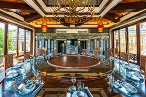 A round dining table with chairs, a chandelier, and a stone wall in the background.