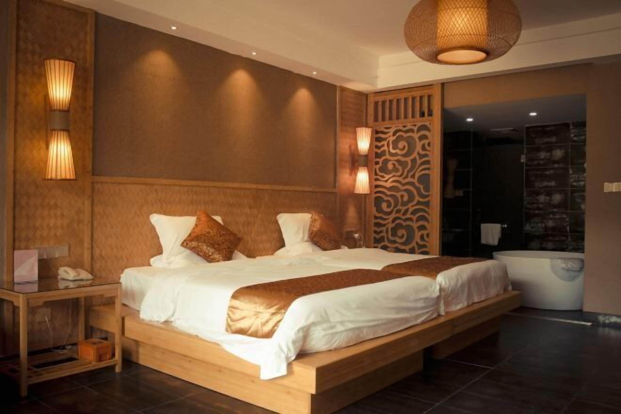 Ein modernes Schlafzimmer mit einem großen Bett, Nachttischlampen, einem Holfnachtkästchen und Blick auf ein Badezimmer.
