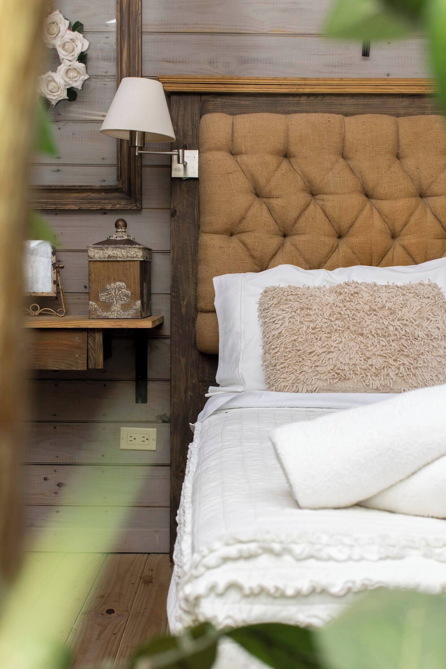 A bedroom with a tufted headboard, a bedside table with a lamp, and a decorative wall piece.