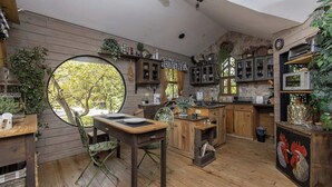 A rustic kitchen with wooden cabinets, a round dining table, and a view through a large window.