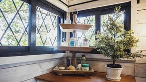 A kitchen counter with a wooden shelf holding various kitchen items, a potted plant, and a tray with food items.