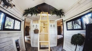 A cozy cabin with a loft bed, a ladder, and a small balcony.