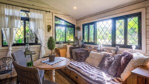 A cozy room with a wooden bench, a round table, wicker chairs, and large windows with curtains.