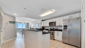A modern kitchen with white cabinetry, a central island, stainless steel appliances, and a view to the outside. - Beach Baby 808/ Beachfront Beauty/ The Beach Club (Gulf Shores)