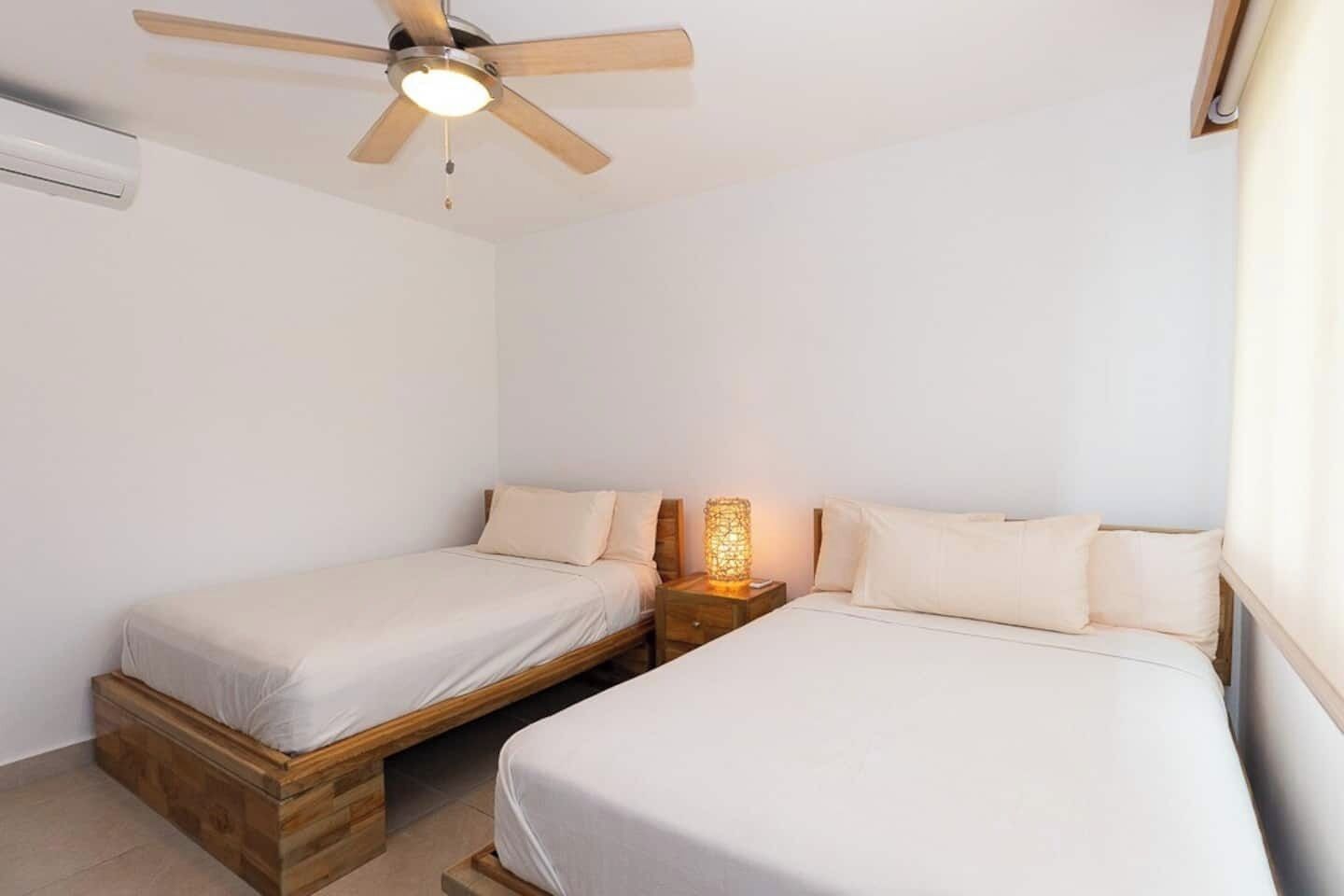 A bedroom with two single beds, a ceiling fan, and a nightstand with a lamp.