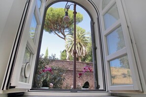 A view through a window with a bell, a tree, and some flowers. - Designer Duplex 2BR 2BA by Colosseum - Historic Center, Metro (Roma)