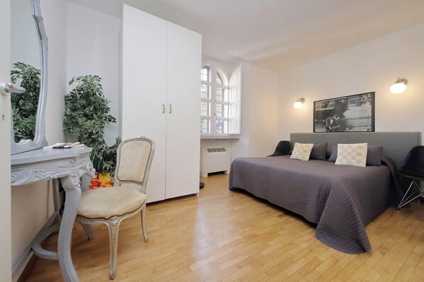 A bedroom with a bed, a desk, a chair, a wardrobe, a window, and a wall-mounted picture.