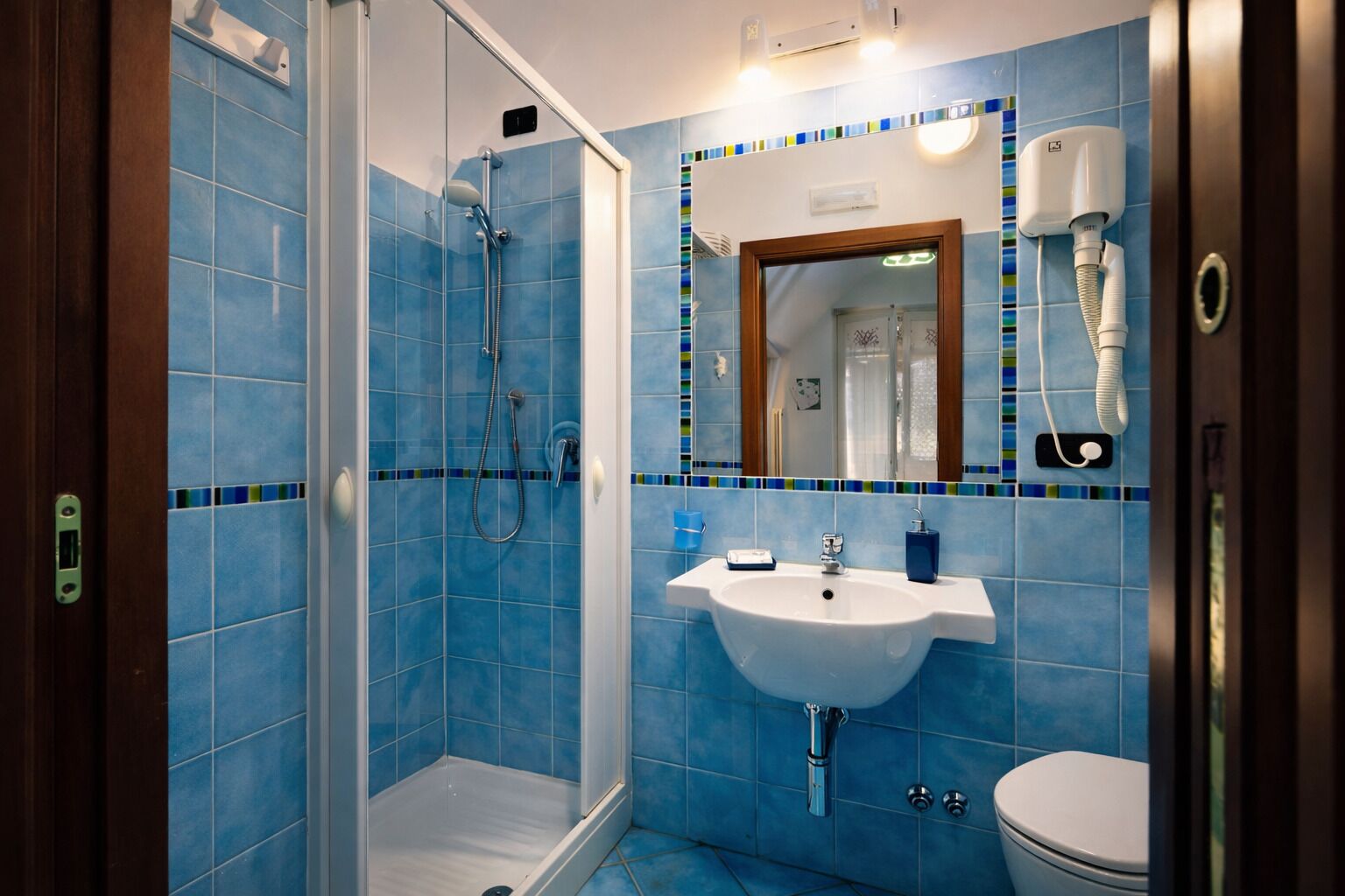 Un baño con ducha, lavamanos e inodoro, con azulejos azules y un espejo.