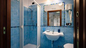 Un baño con ducha, lavamanos e inodoro, con azulejos azules y un espejo.