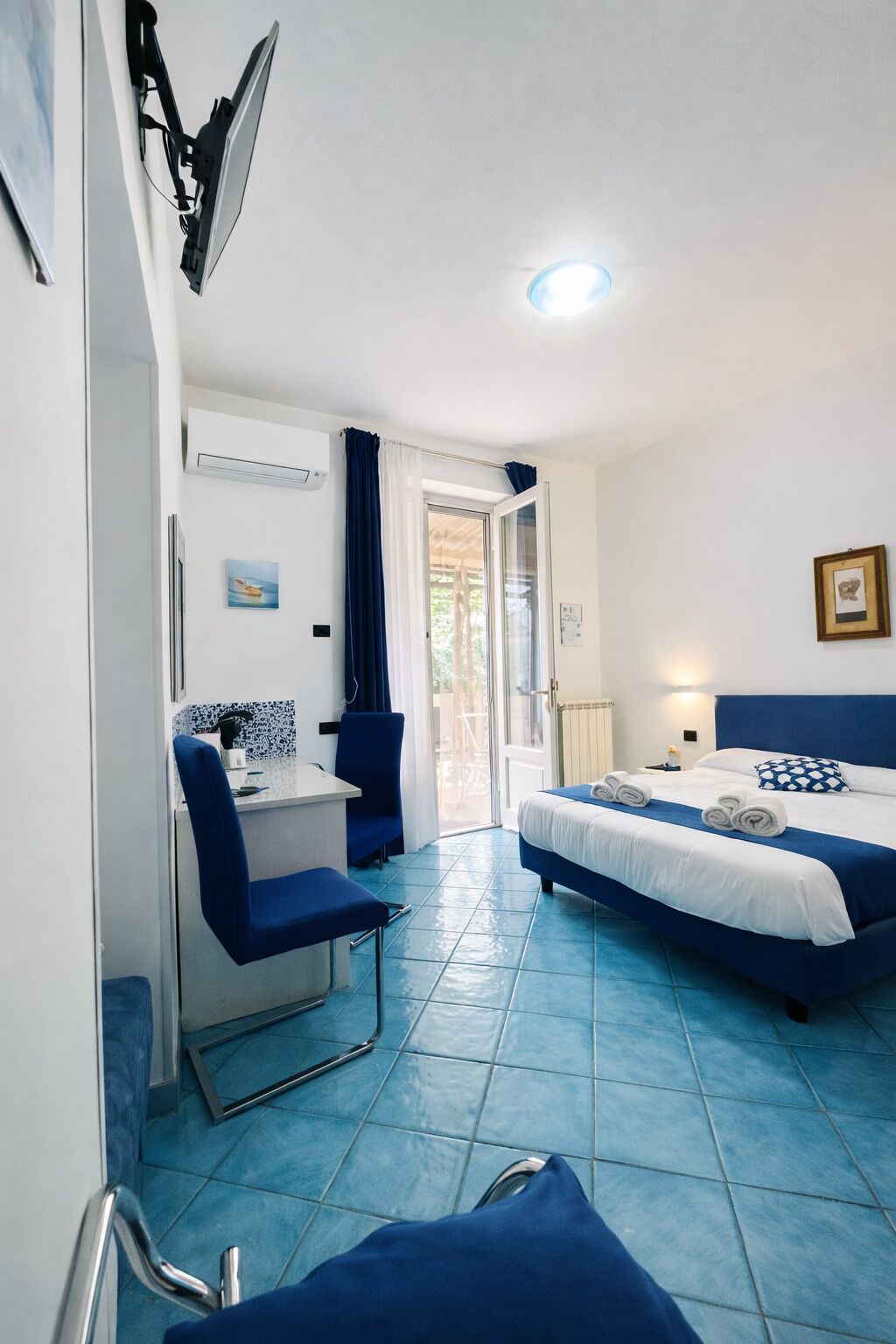 A hotel room with a bed, desk, chair, and a view through a glass door.