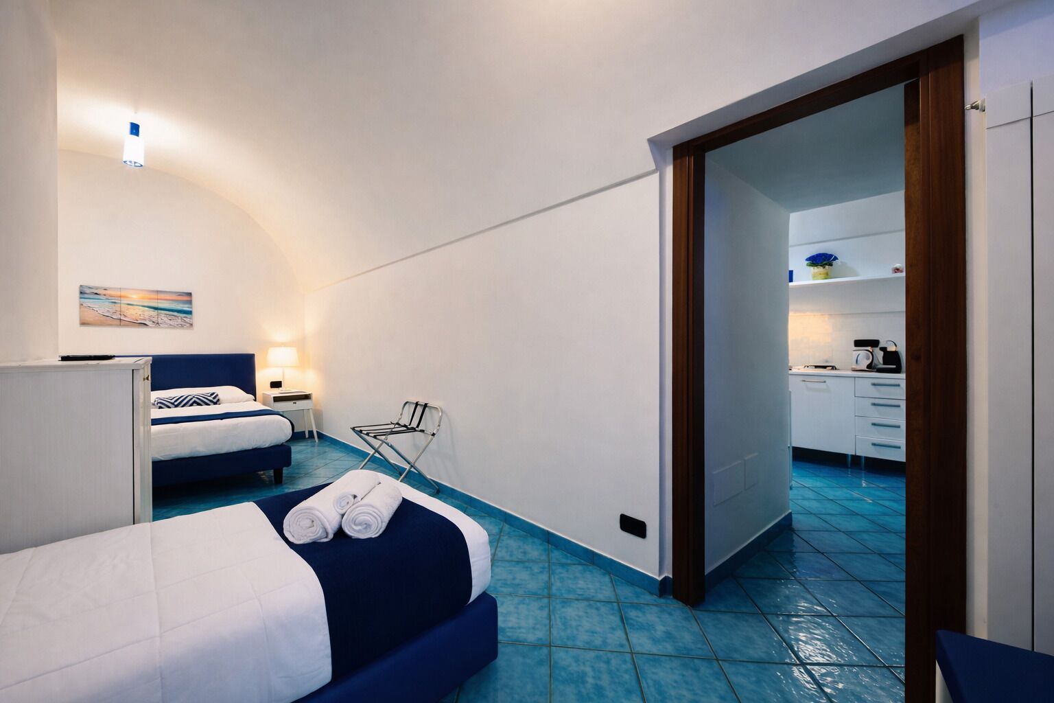 Pieni hotellihuone, jossa on sänky, työpöytä, tuoli ja pieni keittiönurkkaus.
