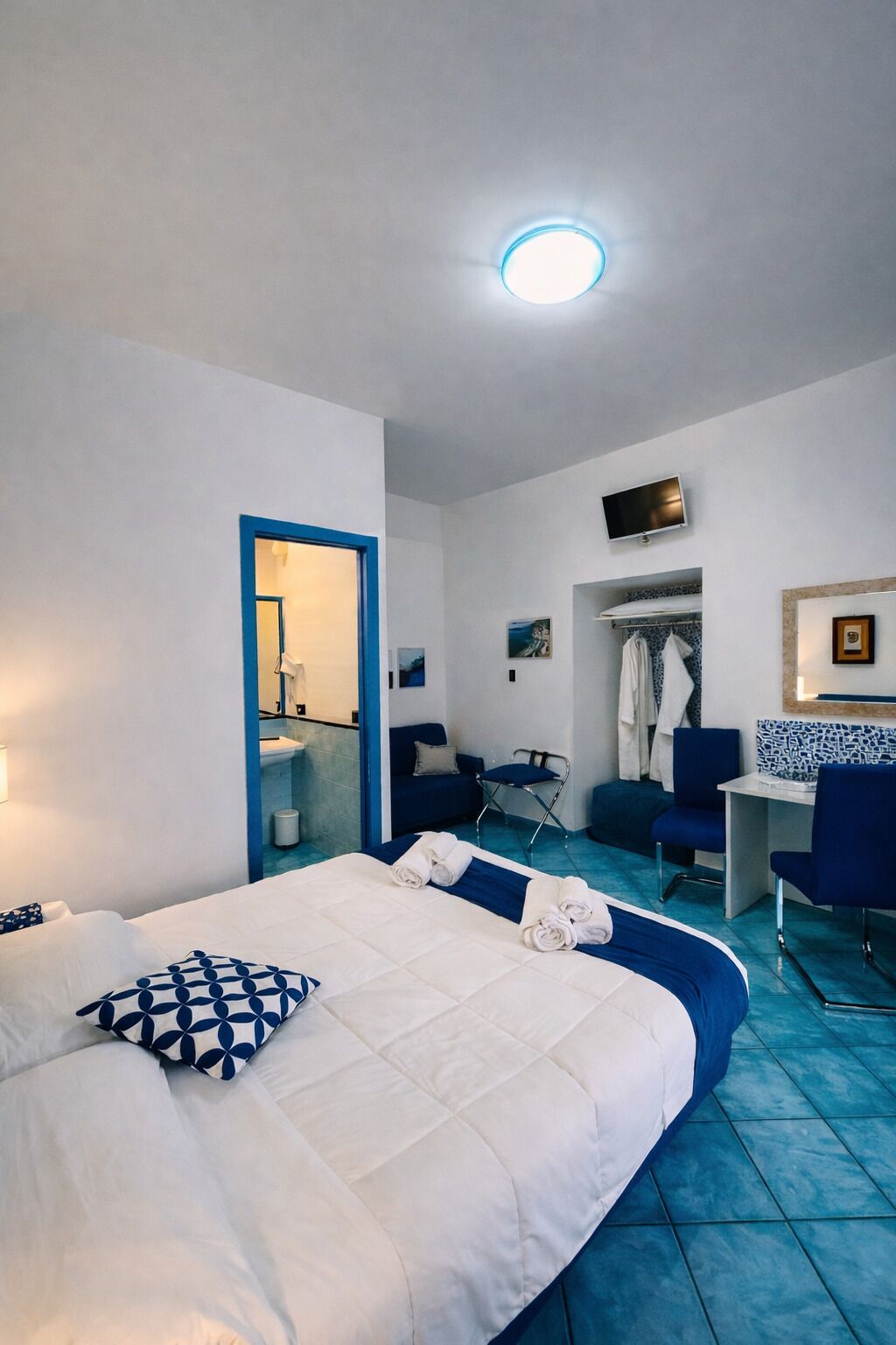 Une chambre d’hôtel avec un lit, un bureau, une chaise, une télévision et une salle de bain visible à travers une porte ouverte.