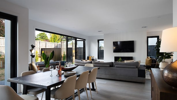 Ein modernes Wohnzimmer mit einem großen grauen Sofa, einem Esstisch mit Stühlen und einem flachbildfernseher an der Wand.