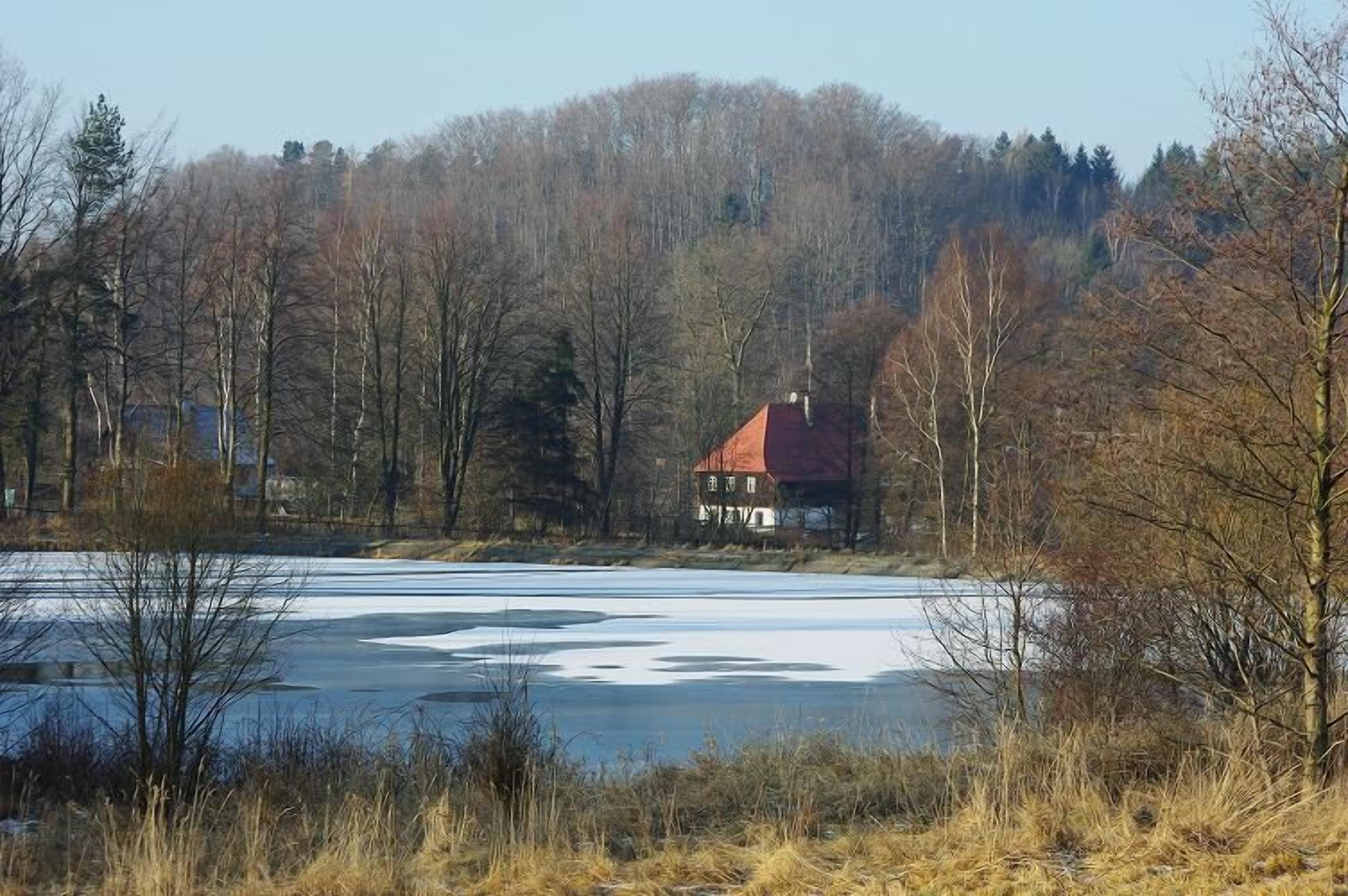 Uma casa com telhado vermelho rodeada por árvores e um lago congelado.