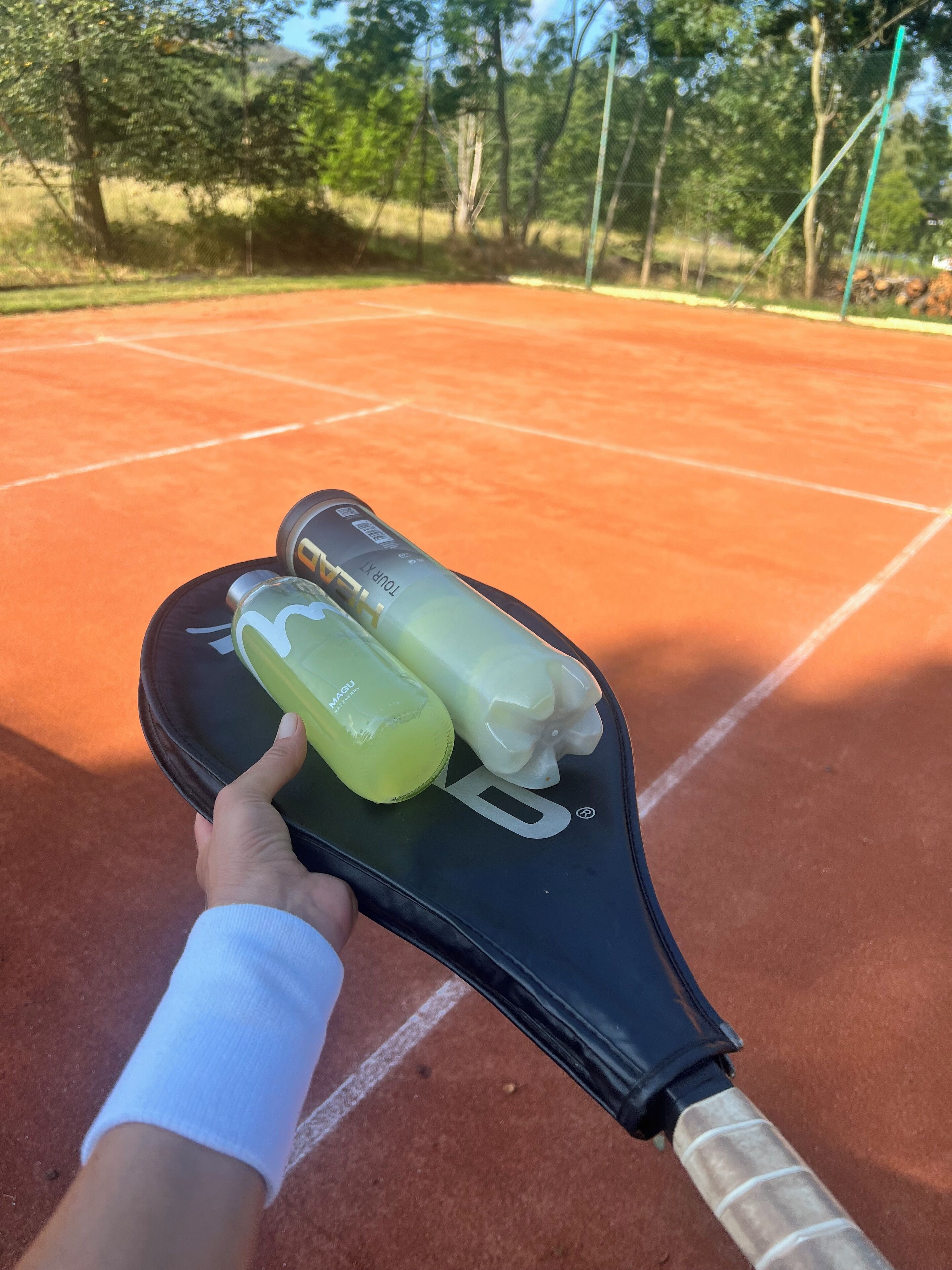 A tennis racket with a grip and two bottles on a clay court.