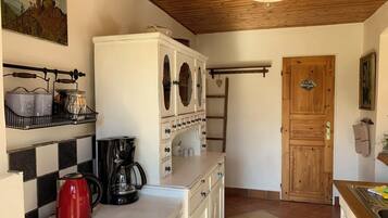 A kitchen with a coffee maker, a red kettle, and a white cabinet with decorative mirrors.