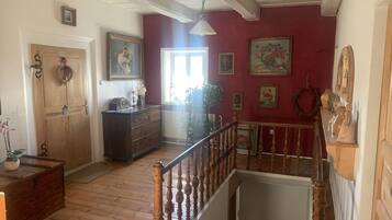 Una habitación con suelos de madera, una escalera con barandilla de madera, un aparador, una puerta y varias fotografías enmarcadas en las paredes.