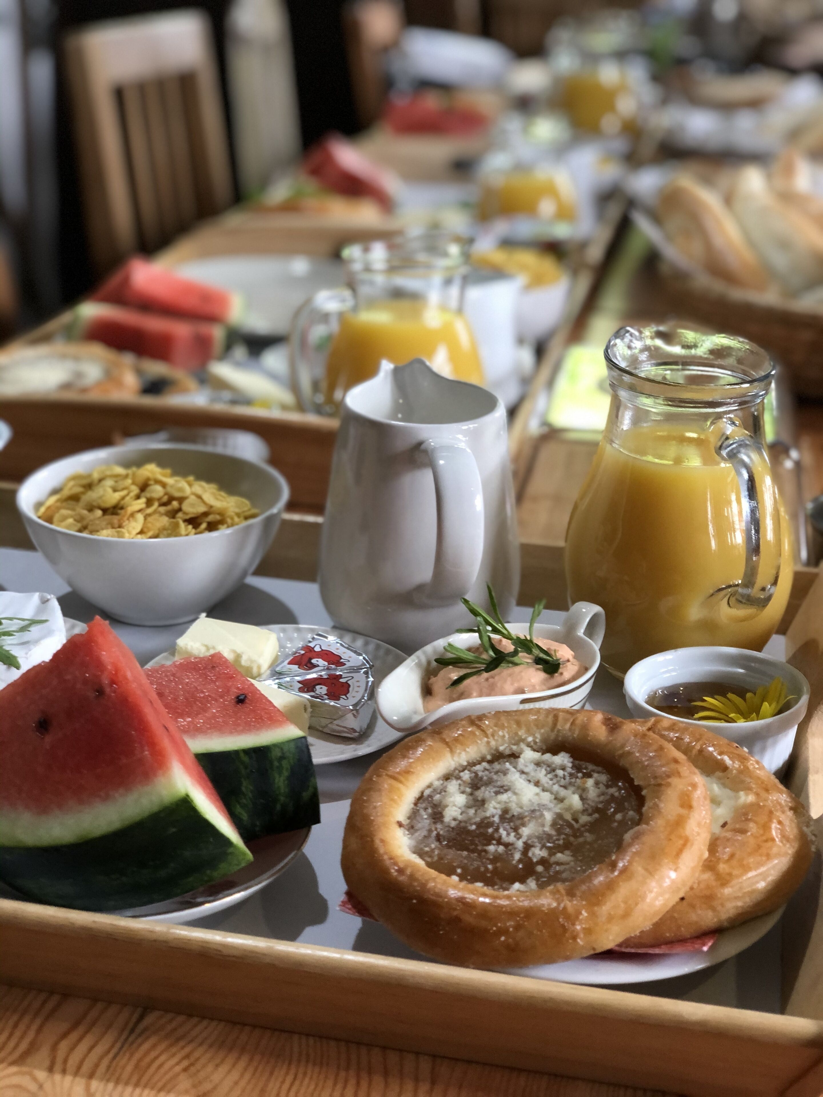Bandeja de desayuno con diversas opciones de comida, como sandía, cereal, tostadas y una jarra de jugo de naranja.