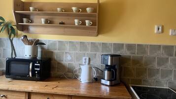 Eine Küche mit Mikrowelle, Kaffeemaschine und einem Regal mit Tassen.