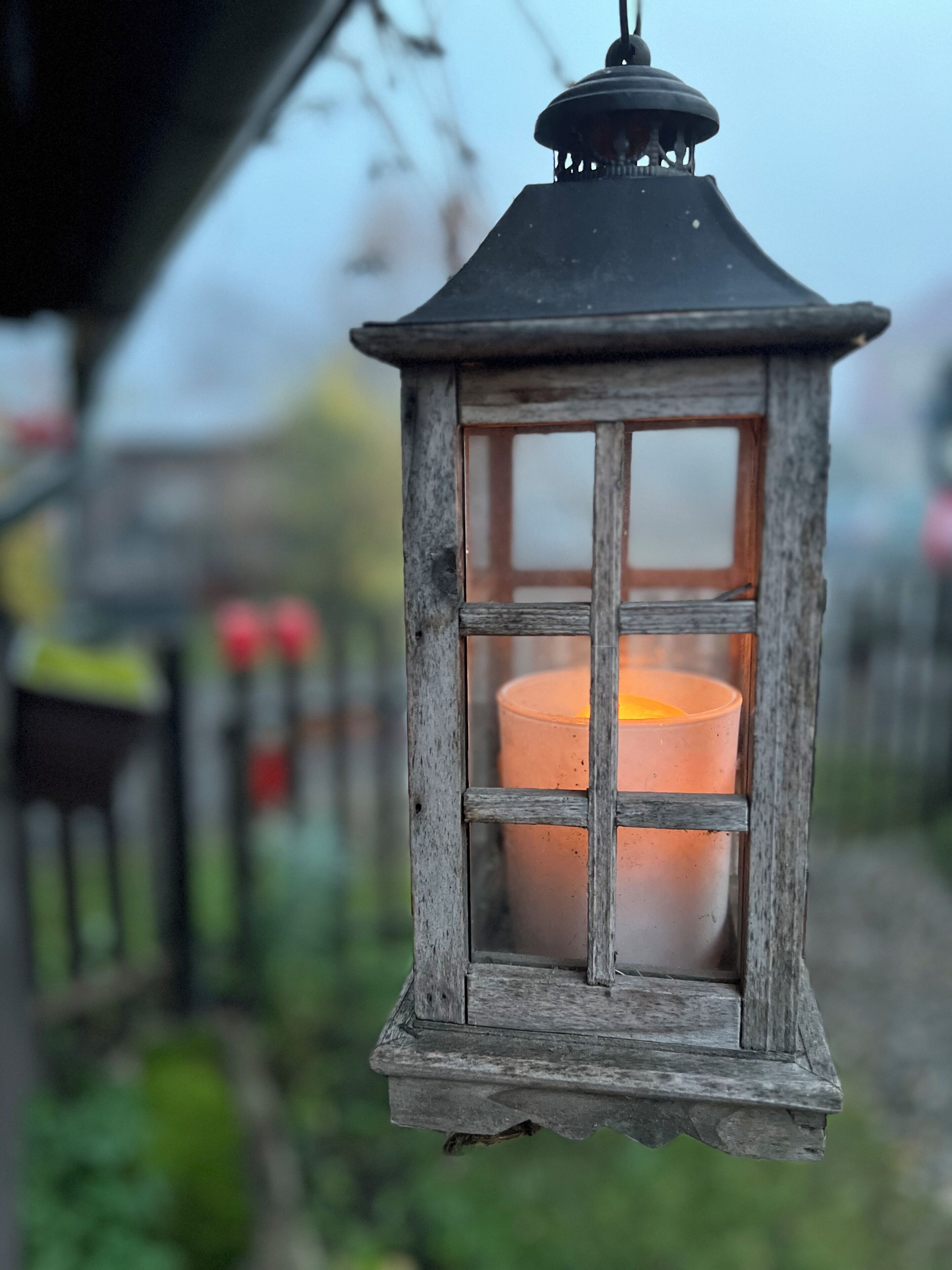 Un farol rústico con una vela en su interior, colgado al aire libre.