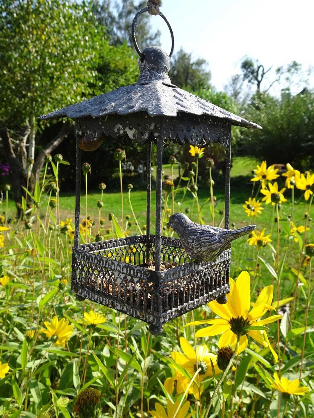 Een vogelhuisje met een vogel erop, omringd door gele bloemen.