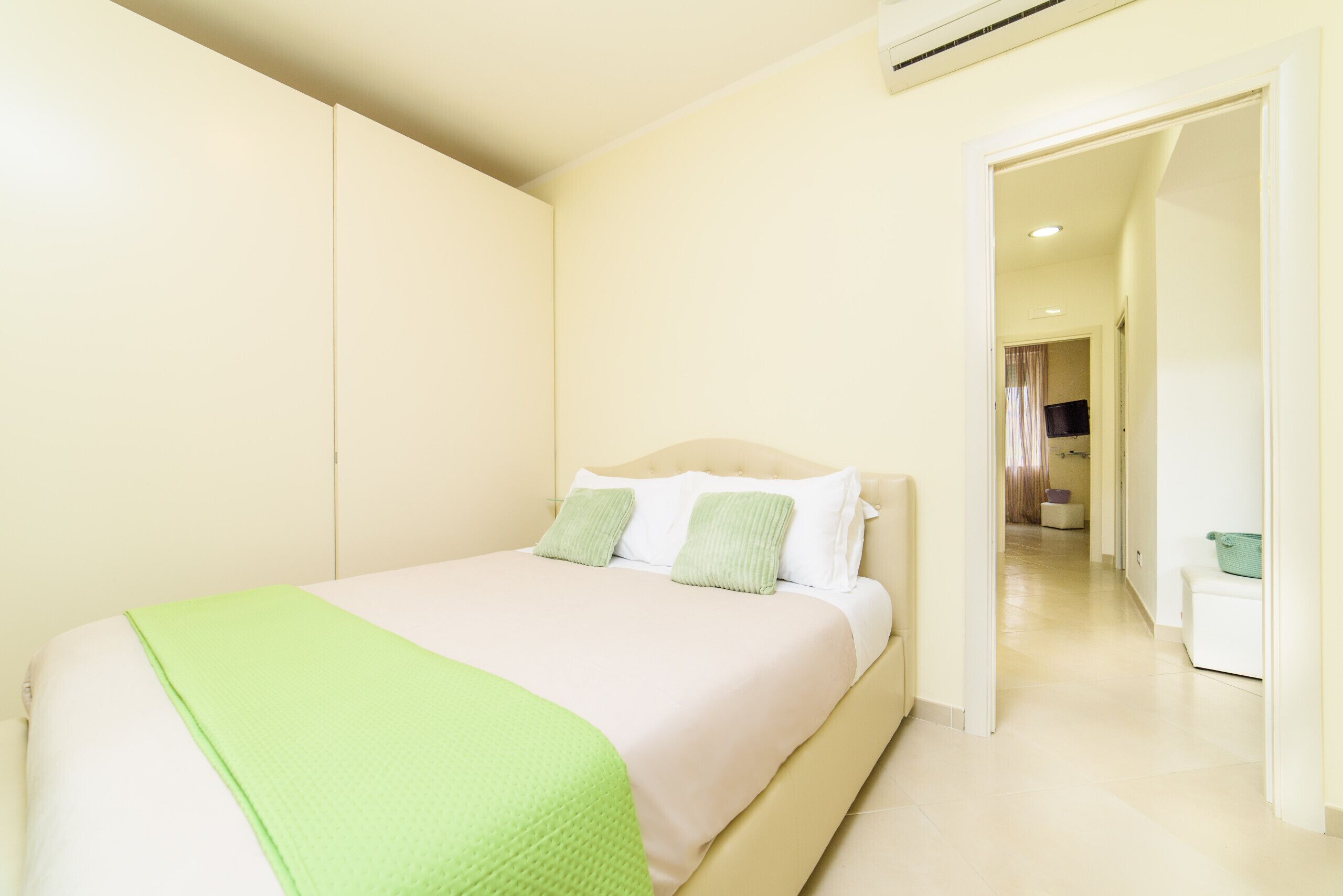 Una camera d'albergo con un letto, una coperta verde e un poggiatesta bianco.
