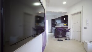 A modern kitchen with dark cabinets, a large window, and two purple bar stools. - Estate4home- L'Onda Viola (Sorrento)