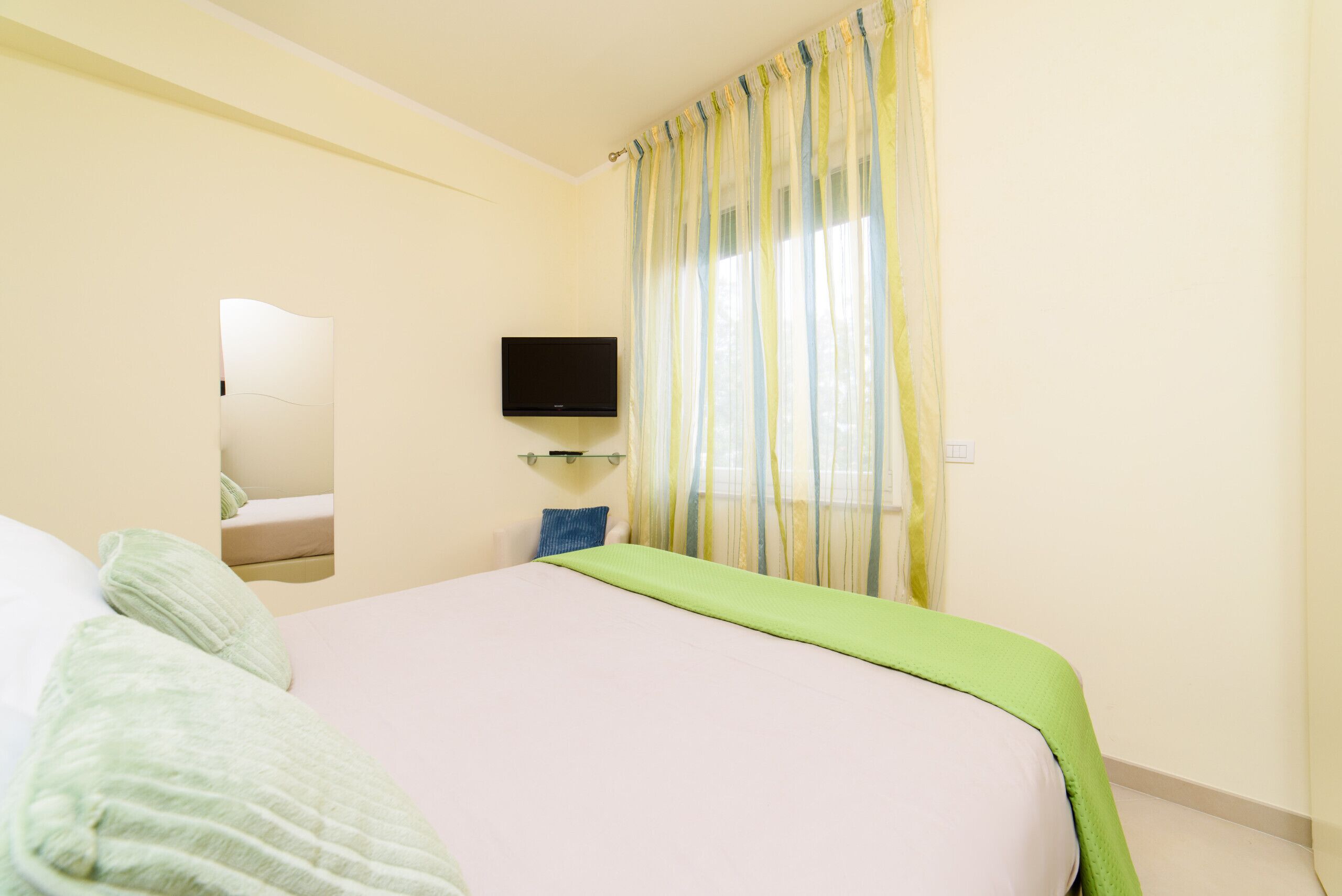 A bedroom with a bed, a television mounted on the wall, and a window with curtains.