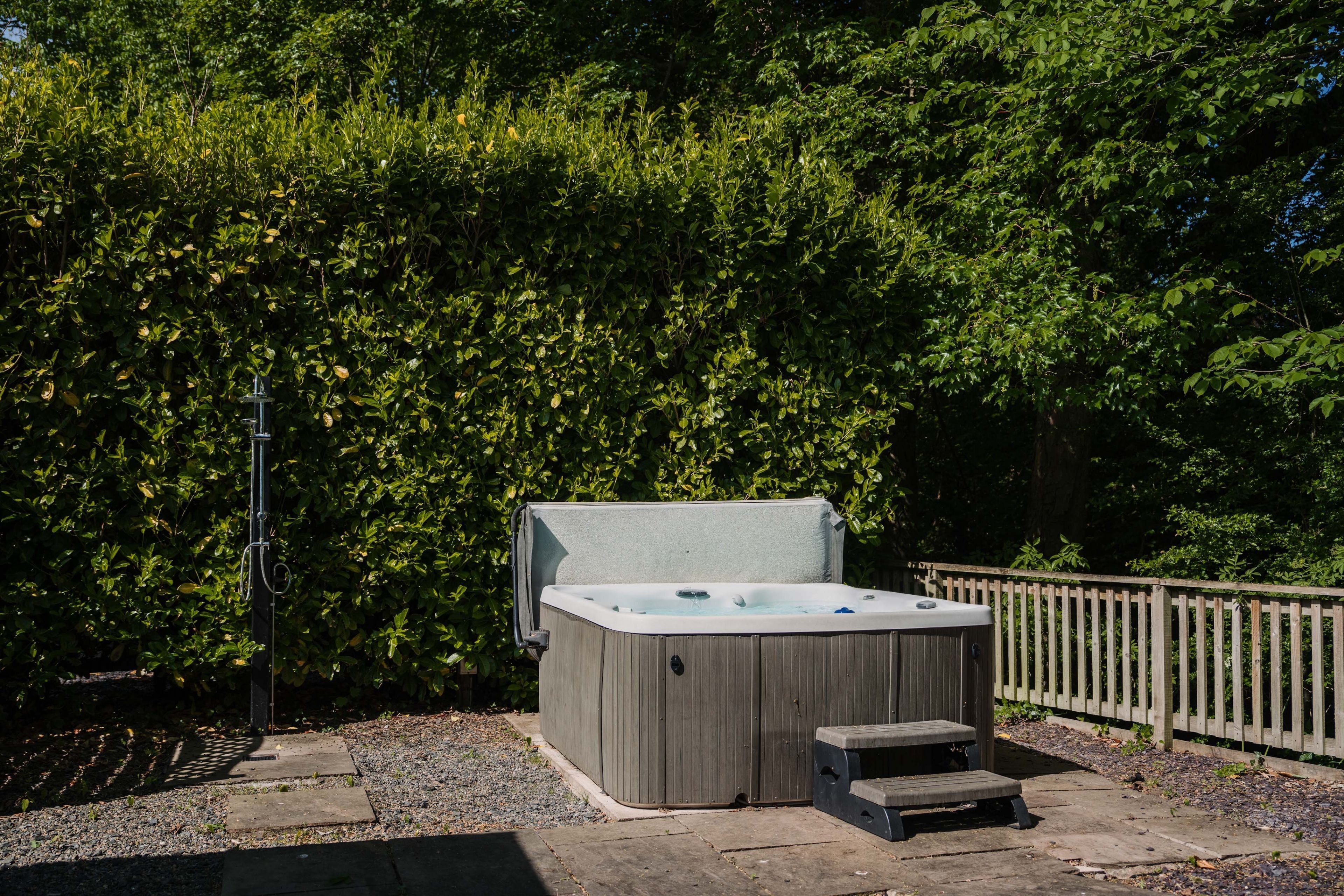 Un bain à remous dans un jardin, avec une clôture en bois et un feuillage dense en arrière-plan.