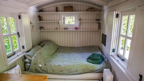 A cozy room with a bed, a small table, and a window with a view of greenery. - Shepherd's hut with hot tub in its own secluded garden (Longtown)