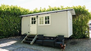 A small, single-story building with a door and windows, a ramp leading to the entrance, and a gravel ground. - Shepherd's hut with hot tub in its own secluded garden (Longtown)