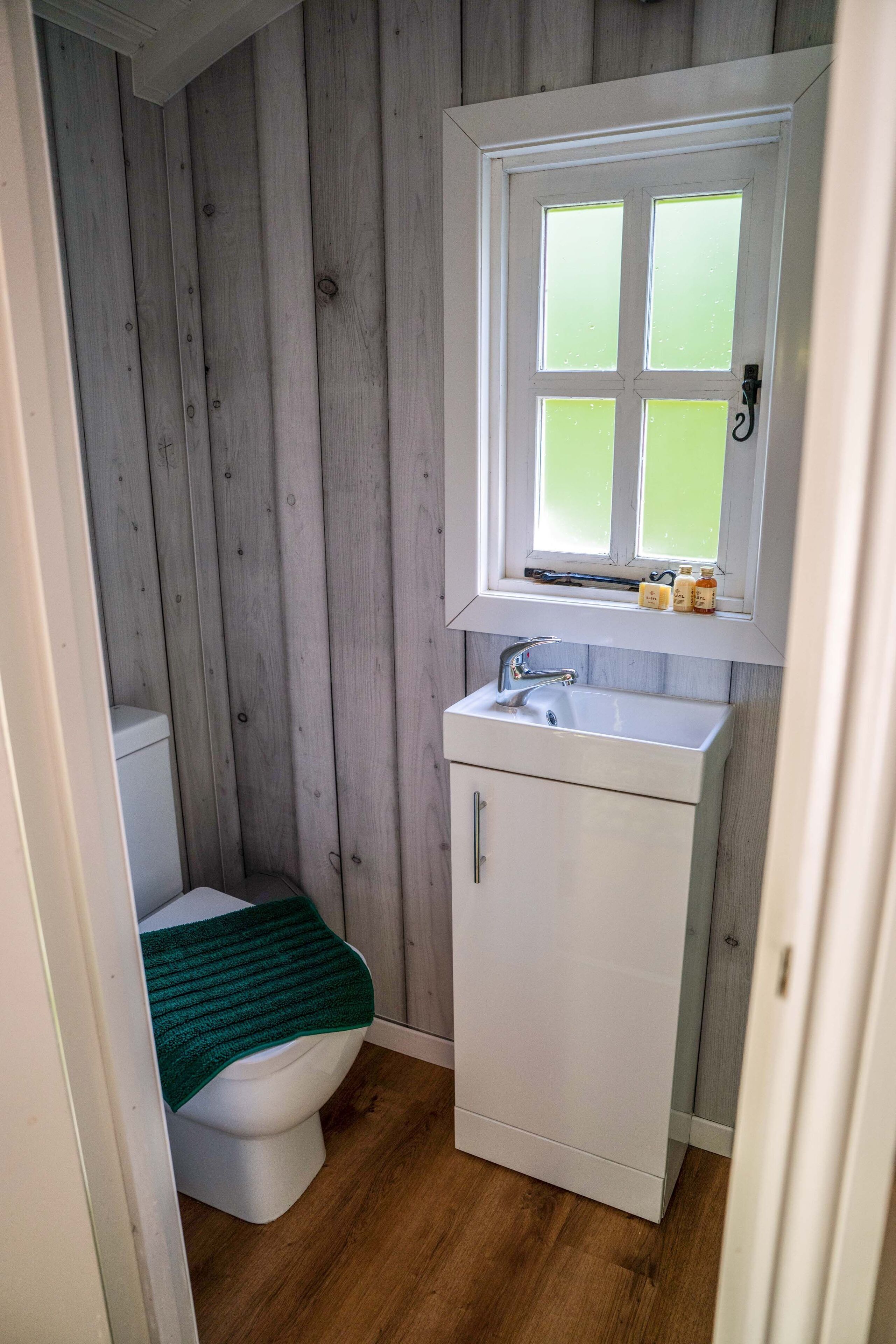A small, compact bathroom with a white toilet, a white sink, and a window above the sink.