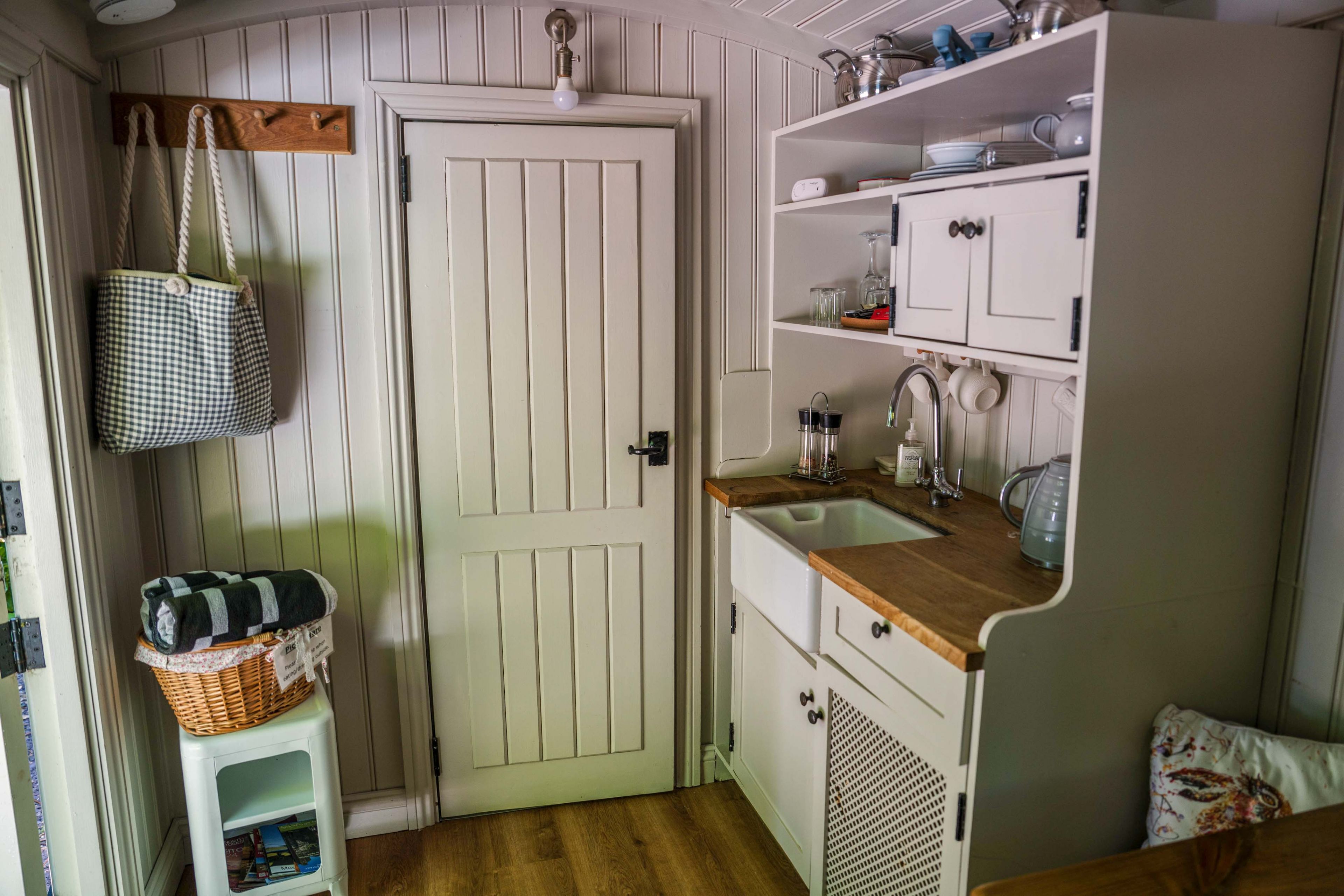 Een compacte keuken met witte kasten, een houten aanrecht en een hangmandje.